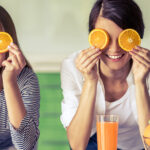 Happy women holding orange slices over their eyes