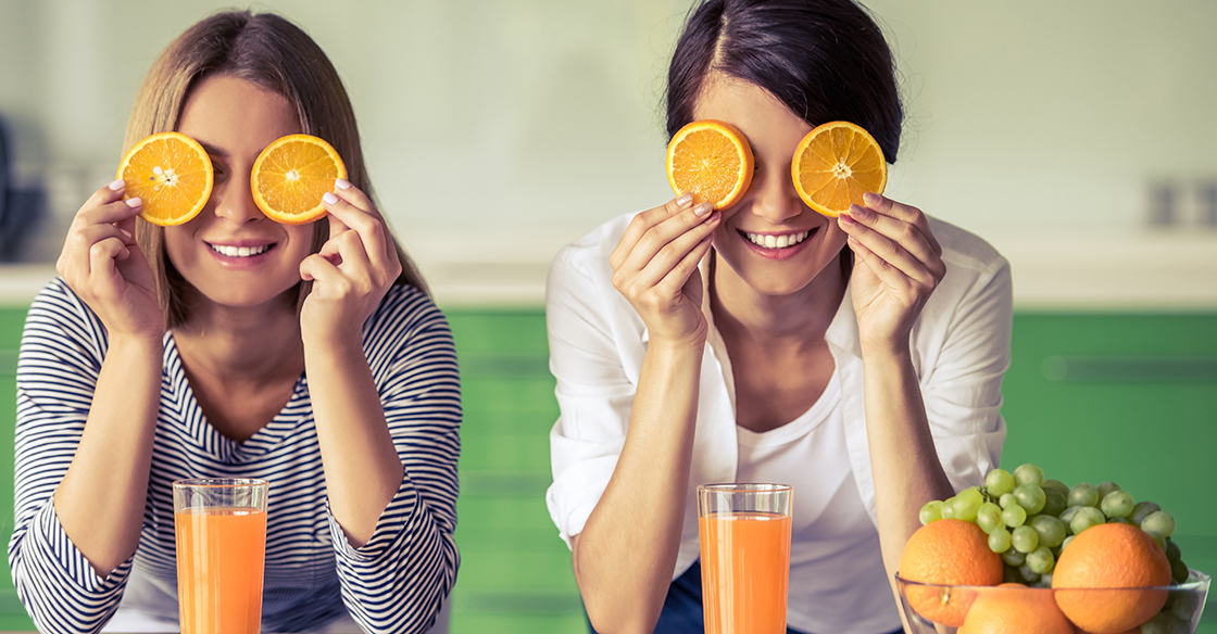 Happy women holding orange slices over their eyes