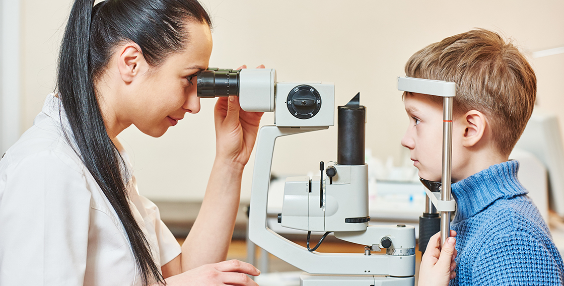 A young boy getting a slit lamp eye examination from an eye doctor